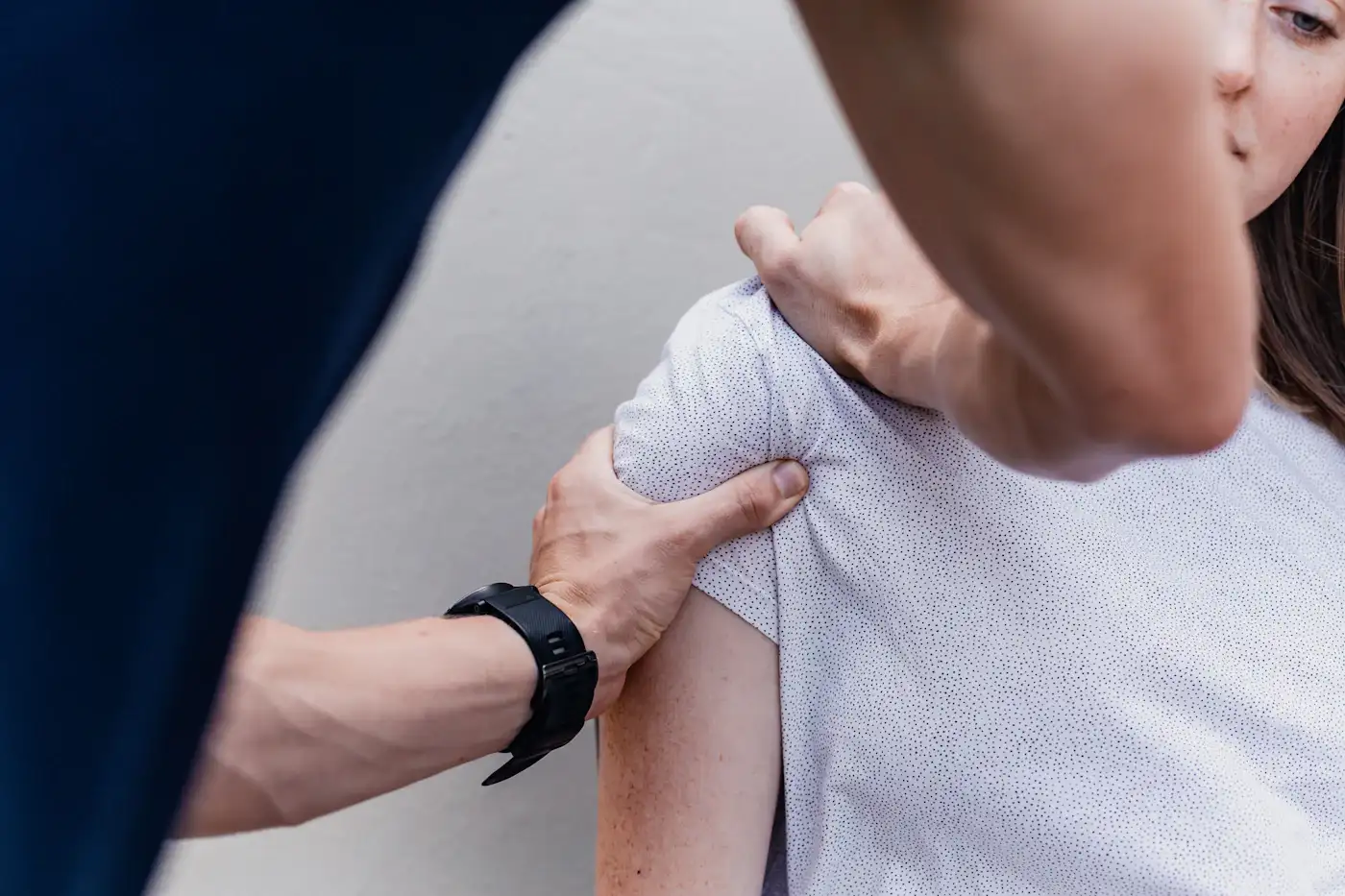 Eine Therapeutin tastet mit beiden Händen die Schulter einer Patientin ab.